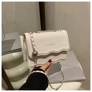 Close-up of beige lychee leather bag with wavy flap and silver chain sphere detail