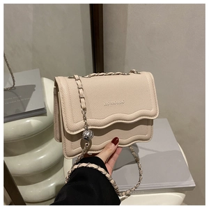 Detail of beige pebble leather handbag with wavy flap and silver spherical chain ornament