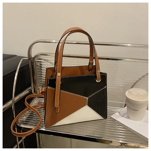 Detail of tricolor patchwork shoulder bag with zigzag stitching on a glass shelf