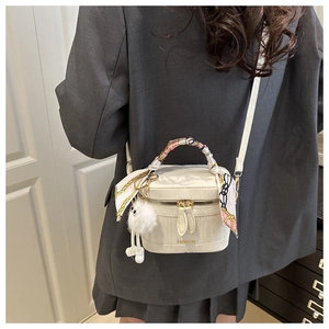 Detail van witte bucket bag met decoratieve zijden handgreep en pluche hanger-accent