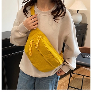 Detail of yellow nylon crossbody bag featuring woven zipper pulls and a curved design