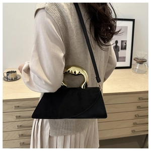 Detail of black suede handbag with unique gold irregular metal handle and shoulder strap
