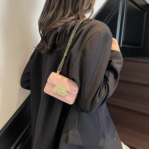 Petit sac bandoulière rose en cuir avec chaîne dorée porté sur un tailleur noir