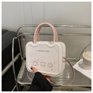 Detail of a creamy white small square bag with pink handles and cute bear illustrations
