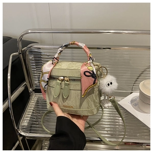Detail van een groene bucket bag met zijden sjaal om handvat en witte pluche hanger