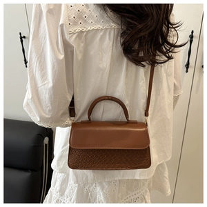 Close-up of brown leather crossbody bag with woven texture worn by model in white lace