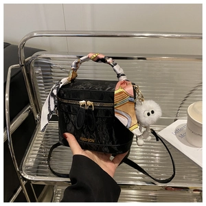 Detail van zwarte bucket bag met textuur, zijden sjaal en witte pluche hanger