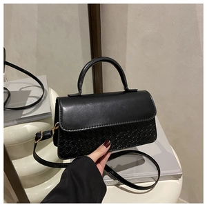 Detail of black woven leather handbag showing smooth flap and golden hardware accents