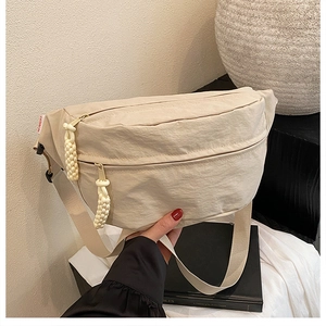 Detail of beige nylon crescent bag with woven zipper pulls and fashion label