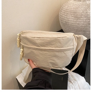 Detail of beige nylon crossbody bag with braided zipper pull and wide shoulder strap