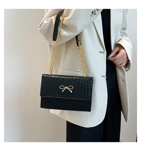 Detail of black woven shoulder bag with golden bow clasp and elegant chain strap on model