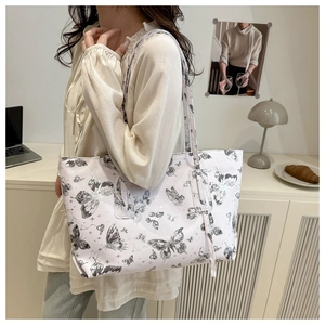 Detail of a large cream tote bag with black butterfly patterns shown on a shoulder