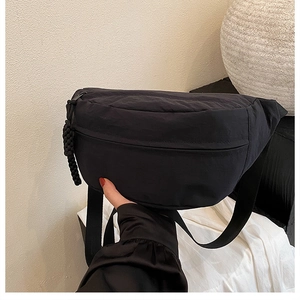 Detail of minimalist black nylon crossbody bag featuring textured fabric and woven zip puller