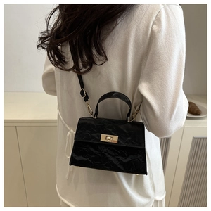 Detail of a black vintage crossbody bag with embossed texture and gold metal twist lock