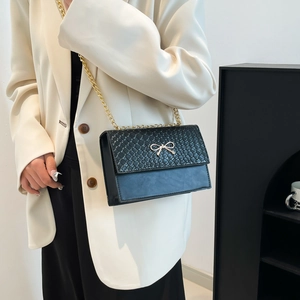 Chic black crossbody bag with woven texture, golden bow detail, and metal chain strap