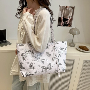 White butterfly print tote bag with long tassels shown on shoulder in cozy indoor setting