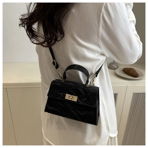 Detail of a black pleated crossbody bag with a golden twist lock on a minimalist model