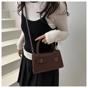 Detail of dark brown leather handbag with decorative buckle and bow on white background