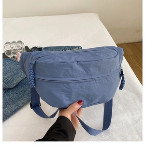 Detail of blue nylon chest bag with dual zippers and woven cord pulls on fabric