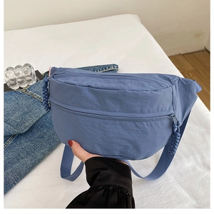 Detailed close-up of a blue nylon crescent crossbody bag with woven zipper pull details