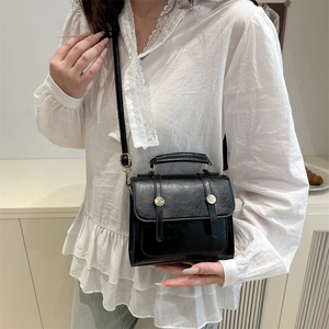 Petit sac à main noir en cuir avec bandoulière et boucles métalliques porté par un mannequin