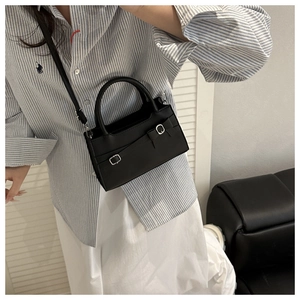 Detail of black leather crossbody bag with buckle straps worn by a model in casual outfit