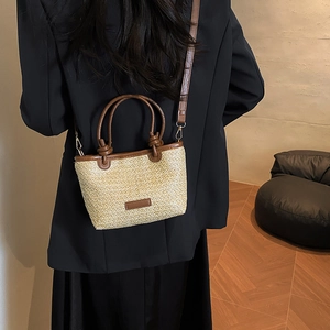 Handwoven straw bucket bag with brown leather handles and a removable shoulder strap