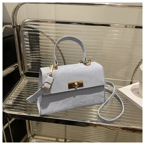 Detail of light blue wrinkled leather handbag with gold metal clasp on a glass shelf