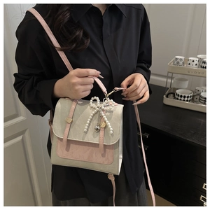 Détail d'un sac carré bicolore avec pendentif nœud en perles et boucles dorées décoratives