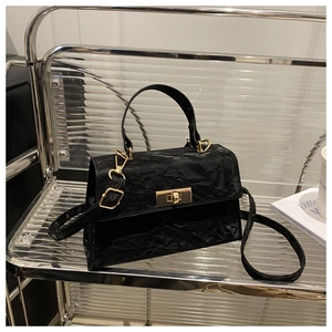 Detail of black pleated crossbody bag with a metal buckle lock on a glass shelf