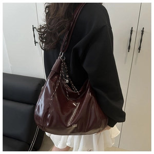 Detail view of burgundy patent leather hobo bag with woven cord charm and logo print