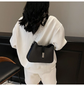 Detail of minimalist black leather underarm bag with silver chain strap on a model