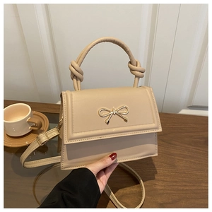 Close-up of beige square handbag featuring a decorative gold bow buckle and knotted handle
