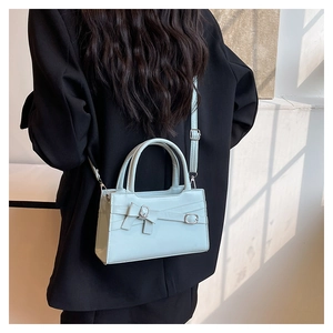 Detail of light blue crossbody bag with bow accent and silver buckle on a black blazer