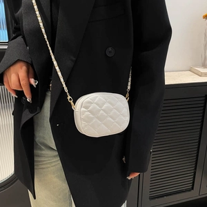White quilted mini round crossbody bag with gold chain strap on professional chic outfit