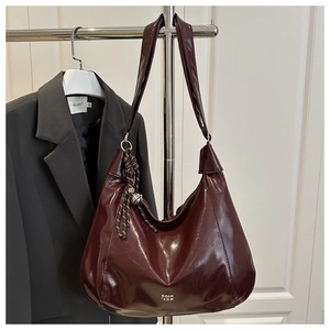 Close-up of shiny dark red leather hobo bag with braided pendant and silver bell detail