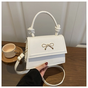 Close-up of a white fashion handbag featuring a golden bow and knotted handle detail