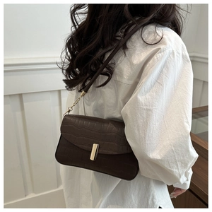 Detail of dark brown faux crocodile leather bag with gold buckle on a white shirt