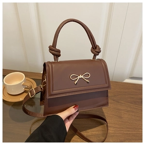 Close-up of brown crossbody bag with gold bow clasp and knotted top handle detail