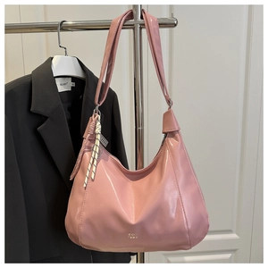 Detail of a pink glossy hobo bag with gold logo and decorative woven rope charm