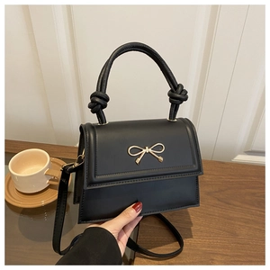 Detail of black mini crossbody bag with golden bow buckle and woven handle on wood desk