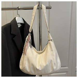 Close-up of white glossy patent leather hobo bag with scarf charm and silver logo detail