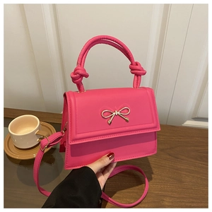 Detail of rose pink handbag with golden bow accent and knotted handle on wooden surface