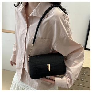 Detail of black crocodile texture shoulder bag with golden buckle on female model