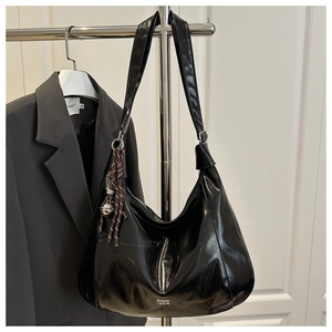 Detail of black patent leather hobo bag with white lettering and side bell charm