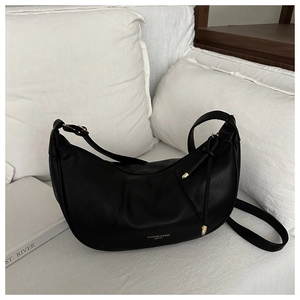 Close-up of black lychee leather crescent bag with golden logo on white sofa