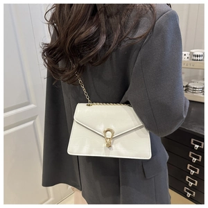Detail of white crocodile-embossed leather bag with golden horseshoe-shaped metal buckle