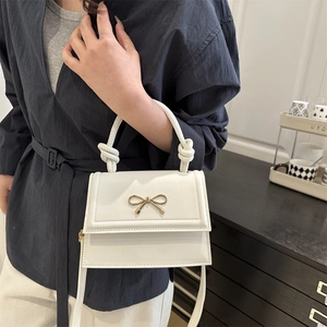 Minimalist white square handbag with metal bow detail and knotted handle shown on a model