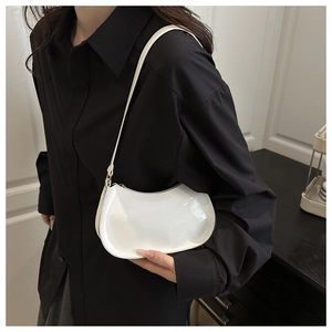 Close-up of a white glossy patent leather half-moon shoulder bag on a black shirt