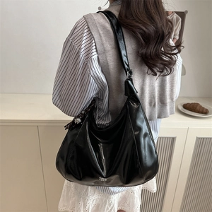 Minimalist black patent leather hobo tote bag shown from a shoulder carry perspective